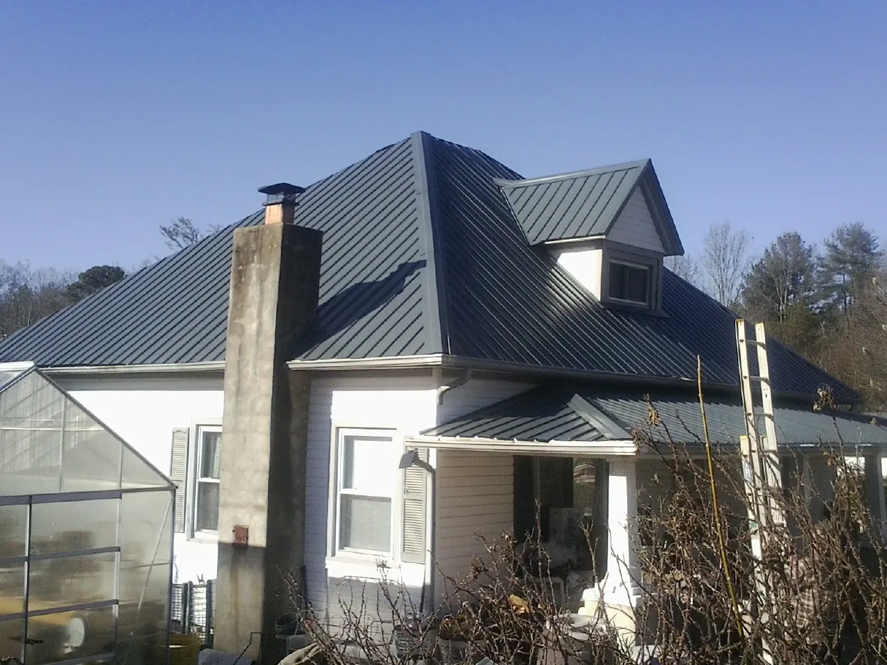 Dark blue standing seam metal roof on a white farmhouse with dormer — Slate & Tile Roof Repair by Roofing Brothers in Gibsonton