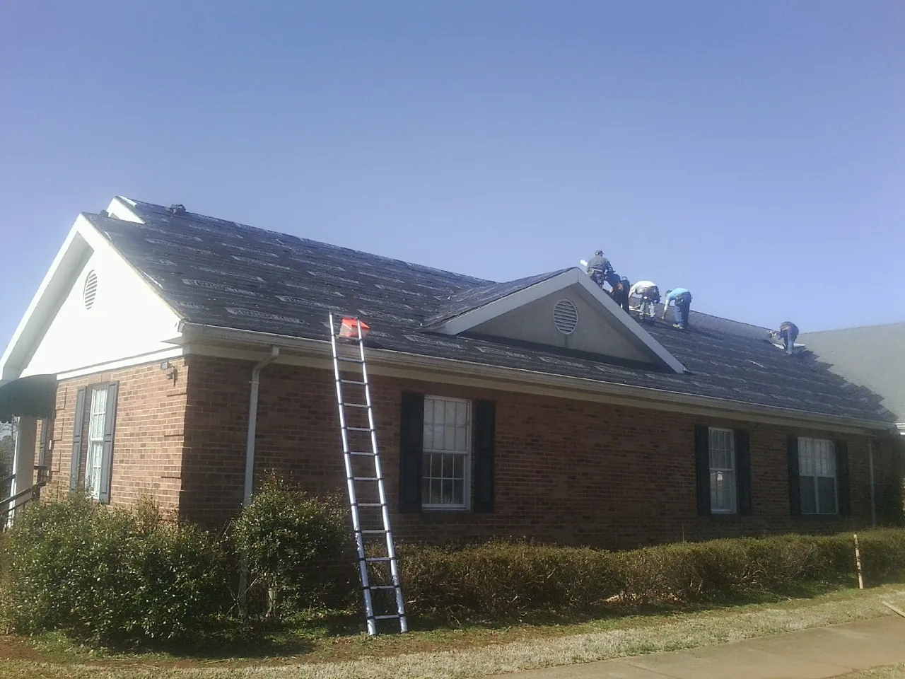 Crew tearing shingles off a brick ranch roof with a ladder set — Emergency Roof Repair work by our crew in Gibsonton