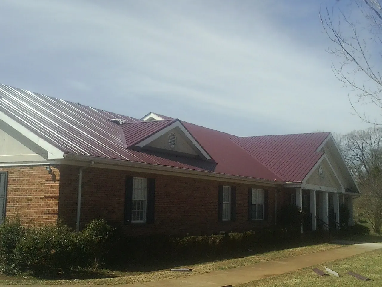 Red metal roof with gabled entries on a long brick building, from a Hail Damage Roof Repair job in Gibsonton