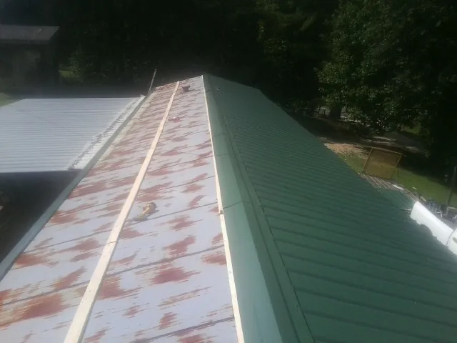 Old rusted panels beside newly installed green metal roofing — Wind Damage Roof Repair by Roofing Brothers in Gibsonton