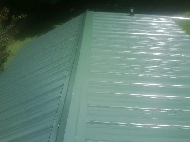 New green metal panels meeting at the ridge of a roof — Flat Roof Repair work by our crew in Gibsonton