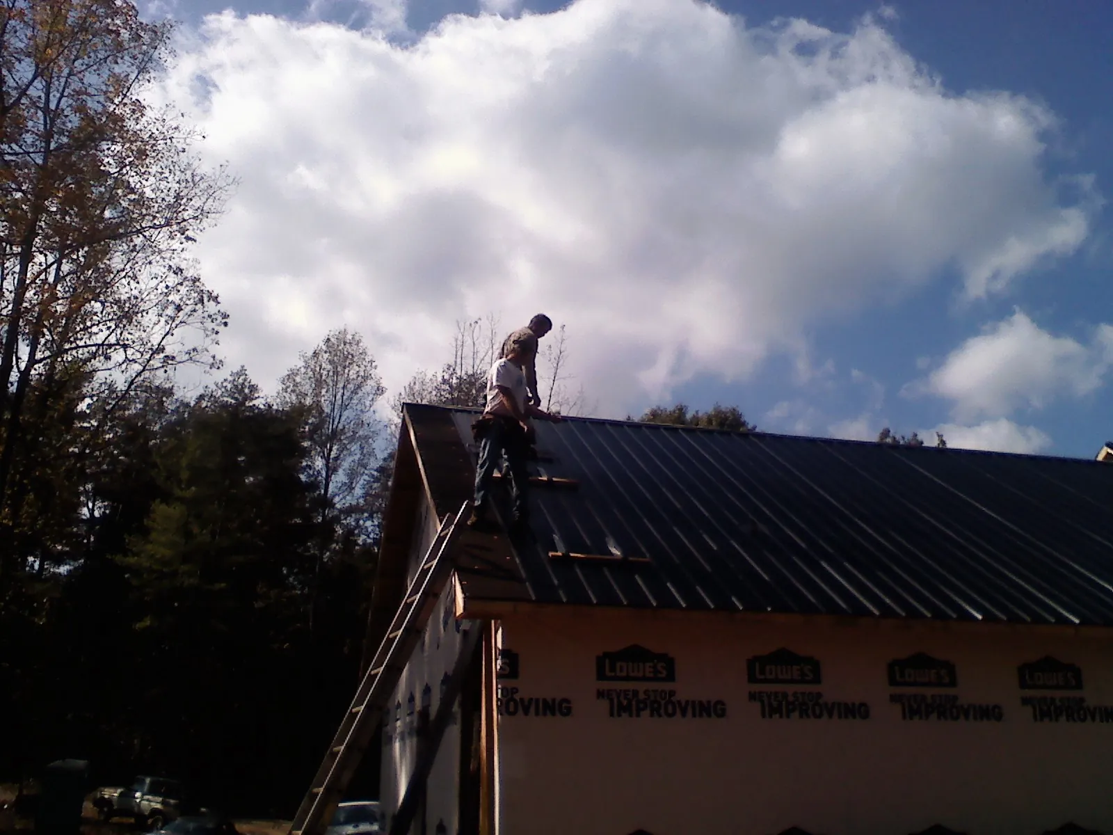 Roofer fastening dark metal panels high against a cloudy sky, from a Roof Inspection job in Gibsonton