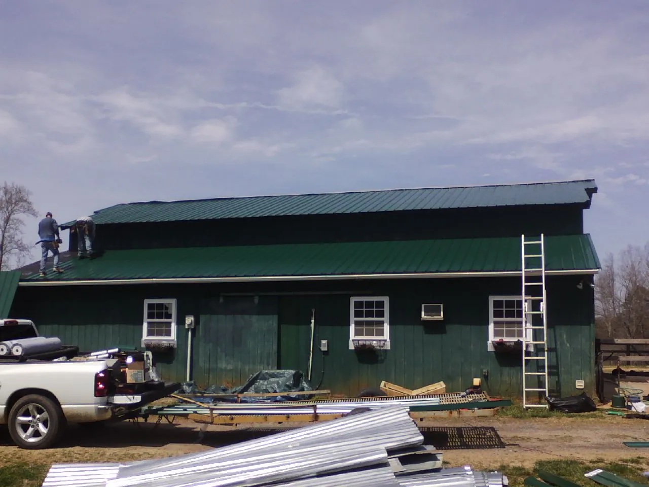 Crew installing green metal roofing on a large green barn in Gibsonton