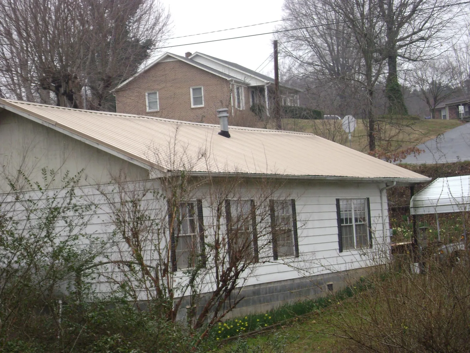 Tan metal roof on a white sided house set into a hillside — Commercial Roofing by Roofing Brothers in Gibsonton